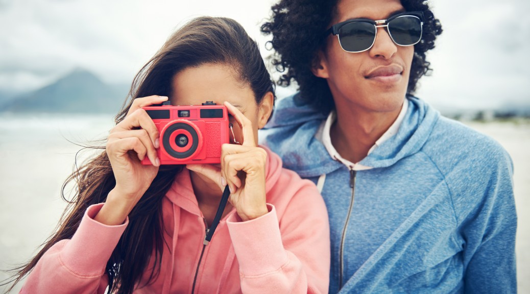 Fashionable hipster couple taking retro camera photo at beach